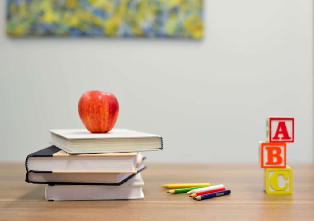 A stack of books, an apple, crayons, and letter blocks on a desk, representing teachers and mental health issues in Ontario