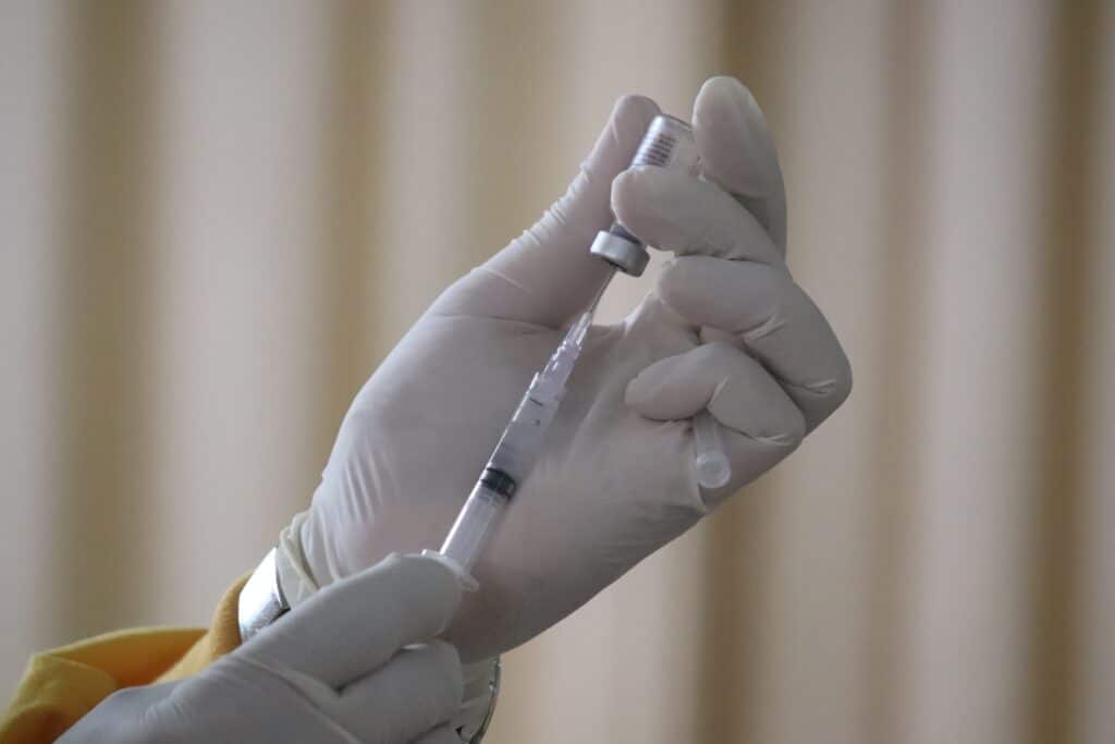 Image of a gloved hand filling a vaccine syrine with medicine, representing mental health issues and COVID-19 vaccine policies