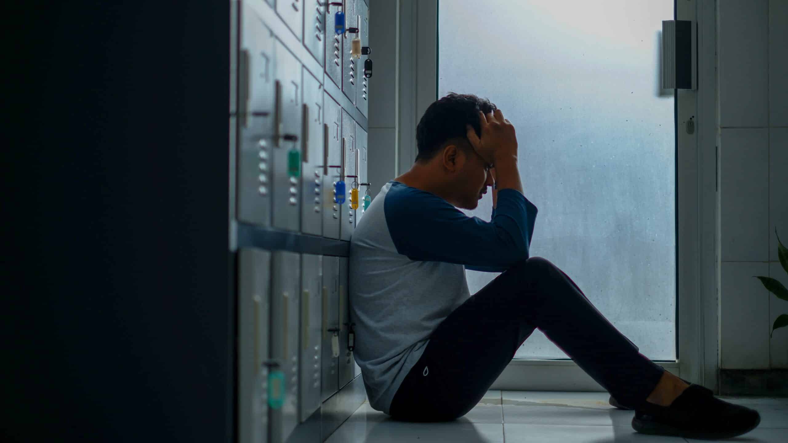 A man sitting against a row of lockers with his head in his hands, representing teachers and stress during the COVID-19 pandemic in Ontario