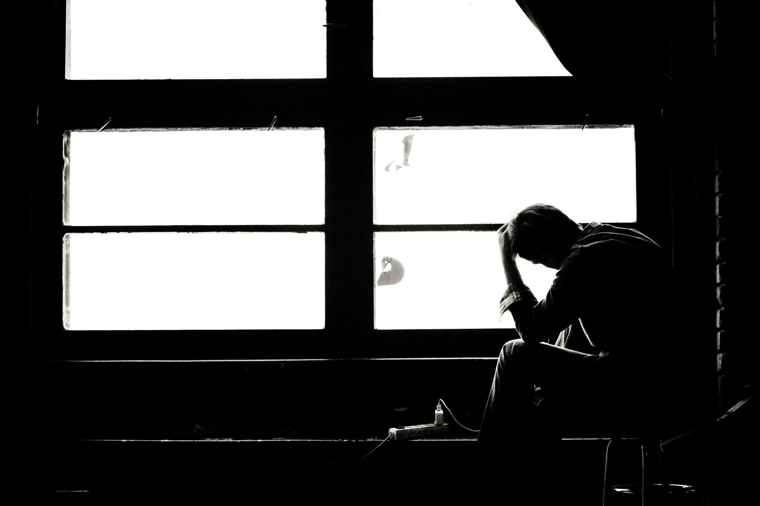Black and white silhouette of a man holding his head in his hand by a window, representing long-term disability denials in Ontario