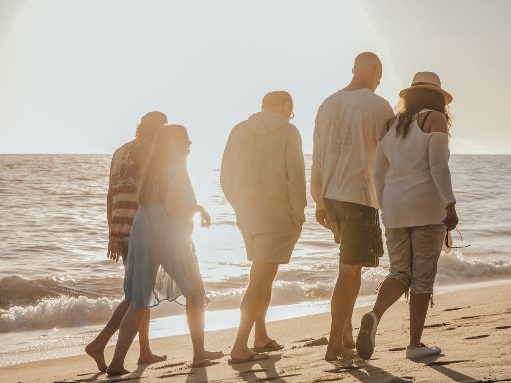 Five friends enjoy a sunny day walking along a sandy beach shore.