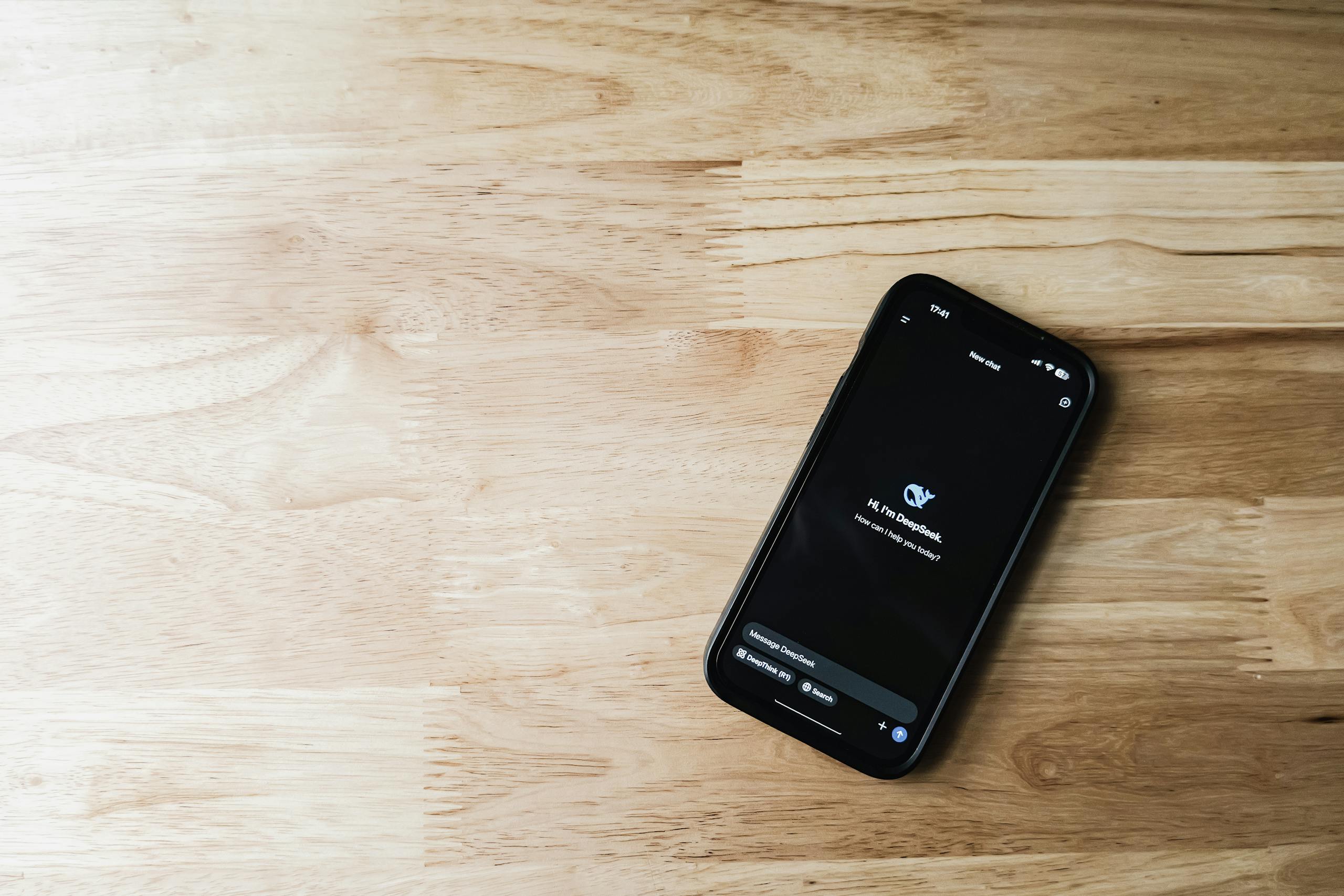 Top-down view of a smartphone displaying a chatbot interface on a light wooden surface.