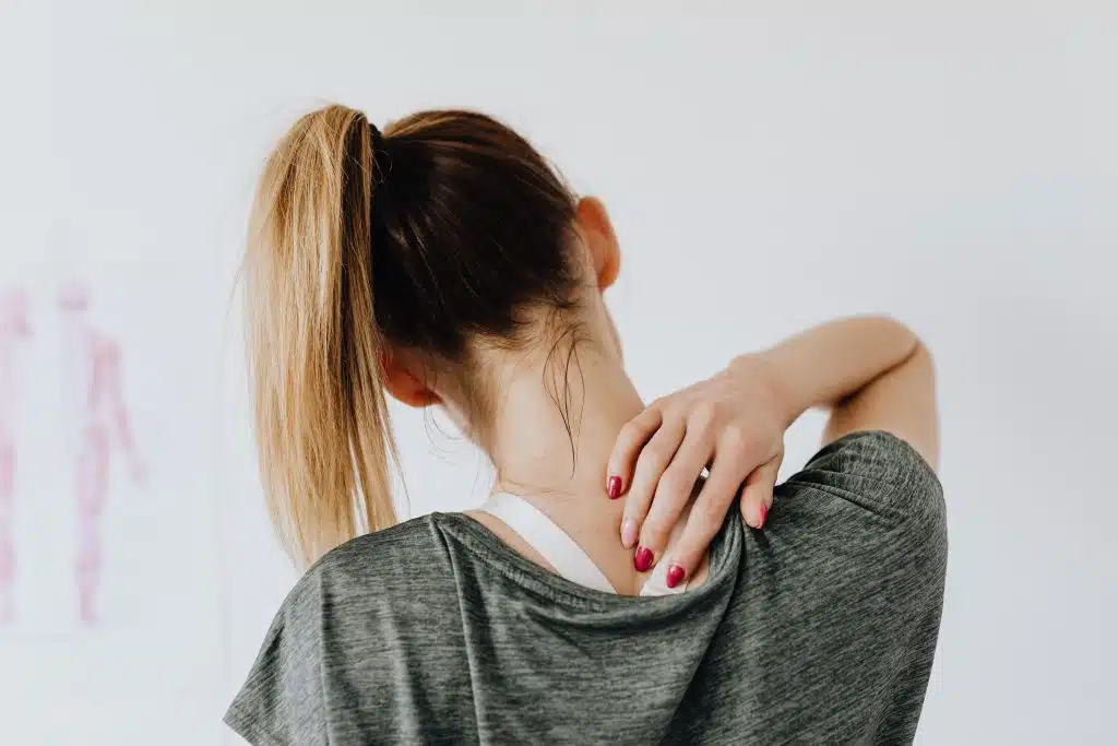 Rear view of a female patient experiencing neck strain and upper back discomfort in a clinic